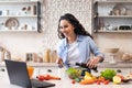 Happy lady watching video recipe on laptop while cooking healthy lunch in kitchen, using computer Royalty Free Stock Photo