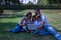 Happy, large family of five sitting on the grass in a park looking at a tablet. With three children, one of them a transsexual Royalty Free Stock Photo