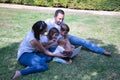 Happy, large family of five sitting on the grass in a park looking at a tablet. With three children, one of them a transsexual Royalty Free Stock Photo