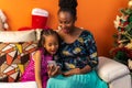 Happy Latin Afro-descendant Colombian mother and daughter sitting on the sofa next to the Christmas tree checking the cell phone