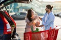 Happy latin couple standing on parking area and loading purchases paper bags after shopping into open trunk Royalty Free Stock Photo