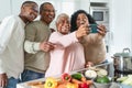 Happy Latin family having fun taking selfie with mobile smartphone while preparing healthy lunch in modern kitchen at home