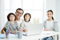 Happy latin father and kids smiling at camera, sitting together at the table at home. Man using laptop, working from Royalty Free Stock Photo