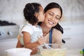Happy latin mother and daughter baking and sharing a kiss while bonding. A young woman helping her daughter bake or cook