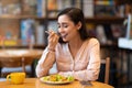 Happy latin woman eating lunch in cafe, enjoying delicious salad with closed eyes and drinking hot beverage. Royalty Free Stock Photo