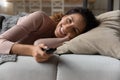 Happy latina female lie on cozy couch hold tv remote Royalty Free Stock Photo