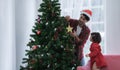 Happy latino family, young bearded father wear santa hat and little daughter decorating a Christmas tree together at home Royalty Free Stock Photo