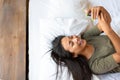 A happy laughing asian woman lies in bed with cell phone. Royalty Free Stock Photo