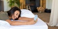 Happy laughing Asian woman lies in bed with mobile phone. She received a declaration of love from her boyfriend. Format Royalty Free Stock Photo