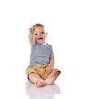 Happy infant baby boy in t-shirt and pants is sitting on the floor pointing at something up on white with copy space