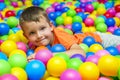 Happy laughing boy having fun in ball pit in kids amusement park and play center. Child playing with colorful balls in playground