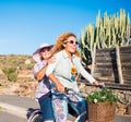 Happy and laughing couple of females enjoying activity. Together on the same vintage bicycle. Blue sky and cactus plants in Royalty Free Stock Photo