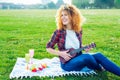 Happy laughing curly hair woman playing ukulele guitar while sitting on lush green grass in a city park at a picnic Royalty Free Stock Photo