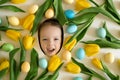 Happy laughing cute baby face surrounded by multicolored  Easter eggs and yellow tulips. Royalty Free Stock Photo