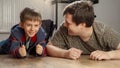 Happy laughing father lying with son on floor and looking at child cheering after winning the game