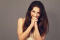 Happy laughing fun beautiful woman covering the mouth the hands with long healthy brown hair on white shirt on grey background Royalty Free Stock Photo