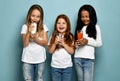 Happy laughing girls friends children in white t-shirts stand holding water, milk or kefir and fresh carrot juice