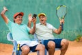 Happy laughing indian senior friends at tennis court by watching mobile phone - concept of taking break, social media Royalty Free Stock Photo