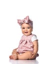 Happy laughing infant baby toddler in polka dot dress and headband with bow sits on the floor holding hand at her leg