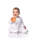 Happy smiling infant baby toddler in white onepiece jumpsuit overall sits on the floor with donut in hands gives it us