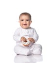 Happy laughing infant baby toddler in white onepiece overall sits on the floor holding donut in hands