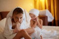 Happy laughing kids, boy and girl in soft bathrobe after bath play on white bed with white pillows in sunny bedroom. Child in Royalty Free Stock Photo