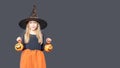 A happy laughing little girl in a carnival witch costume holds a Halloween pumpkin baskets for treats on a dark Royalty Free Stock Photo