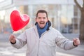 Happily laughing handsome man with a red heart shaped air ballon standing in a city street Royalty Free Stock Photo