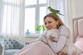 Happy laughing mature woman and green parrot at home in bed Royalty Free Stock Photo