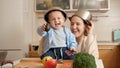 Happy laughing mother with baby son playing on kitchen with cooking pans on heads. Concept of little chef, children cooking food, Royalty Free Stock Photo