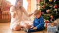 Portrait of happy laughing mother with toddler boy sitting next to Christmas tree at morning Royalty Free Stock Photo