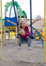 Happy laughing preschool girls swinging on a swing with arms apart on a playground, vertical Royalty Free Stock Photo