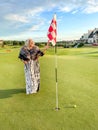 Happy laughing senior woman plays golf on golf course in evening attire. Ball is near hole with flag Royalty Free Stock Photo