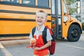 Happy laughing smiling Caucasian boy student by yellow bus on first September day. Hard of hearing child kid eating apple fruit at Royalty Free Stock Photo