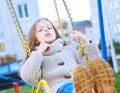 Happy laughing teen girl with long hair wearing a knitted cardigan enjoying a swing ride on a sunny autumn playground in Royalty Free Stock Photo