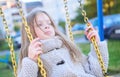 Happy laughing teen girl with long hair wearing a knitted cardigan enjoying a swing ride on a sunny autumn playground in Royalty Free Stock Photo