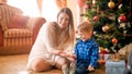 Happy laughing toddler boy with beautiful young mother on floor covered with colorful confetti next to Christmas tree Royalty Free Stock Photo
