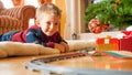 Happy laughing toddler boy lying on floor and looking on toy railroad around big Christmas tree