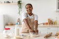 Happy laughing young black female in apron making dough, enjoy cooking pie in contemporary light kitchen
