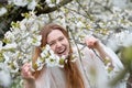 Happy laughing young redhead woman portrait, spring positive emotions in blooming tree blossoms