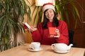 Happy laughing young woman in santa hat opens christmas gift in the morning at breakfast. Positive emotions and holiday Royalty Free Stock Photo