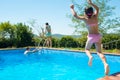 Happy little active girl jumping into outdoor swimming pool during family summer vacation