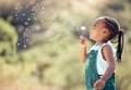 Happy little african american girl blowing a flower in outside. Cheerful child having fun playing and blowing a Royalty Free Stock Photo