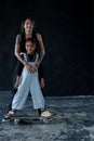 Happy little African kid boy and Asian young cool woman teacher with tattoo hugging and standing on skateboard on black background