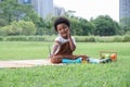 Happy little African kid boy holding a brush to paint in book while sitting on picnic mat in park Royalty Free Stock Photo