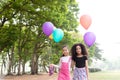 Happy little asian & african american girl playing colorful balloons together. Trees and green gardens background. Smiling lovely Royalty Free Stock Photo