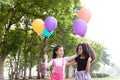 Happy little asian & african american girl playing colorful balloons together. Trees and green gardens background. Smiling lovely Royalty Free Stock Photo