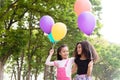 Happy little asian & african american girl playing colorful balloons together. Trees and green gardens background. Smiling lovely Royalty Free Stock Photo