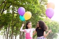 Happy little asian & african american girl playing colorful balloons together. Trees and green gardens background. Smiling lovely Royalty Free Stock Photo