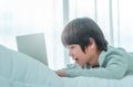 Little Asian boy is using laptop computer on his bed in his room in daytime by the windows Royalty Free Stock Photo